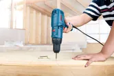 Una persona utiliza un taladro con cable para fijar un tornillo en la madera.