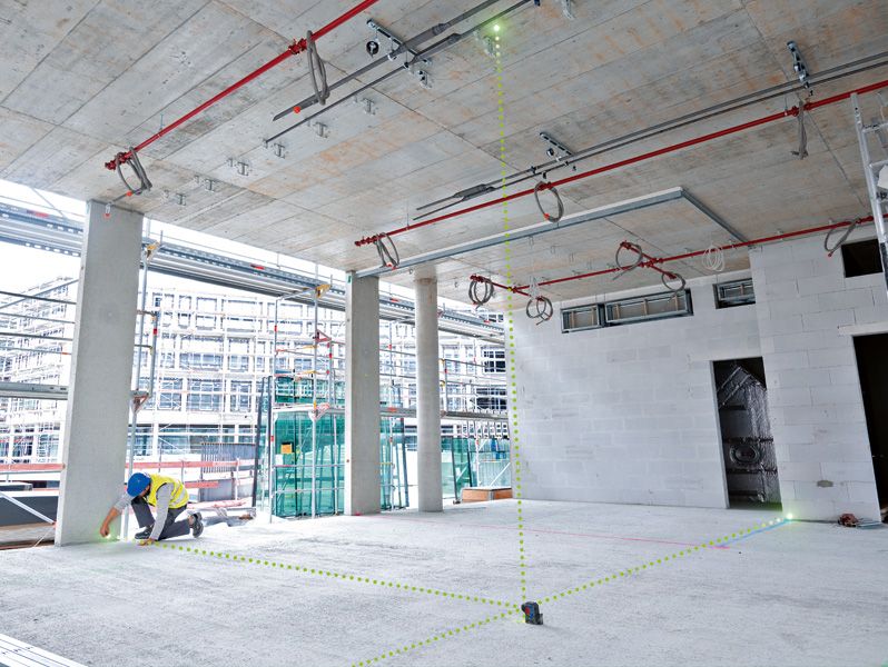 Una persona que usa equipo de seguridad utiliza una herramienta niveladora láser para alinear puntos en un área de construcción.