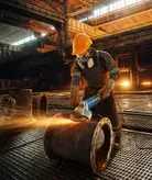 Una persona que usa equipo de seguridad muele un tubo grande de metal, produciendo chispas.