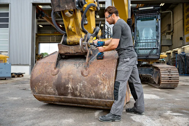 Una persona que usa equipo de seguridad utiliza una llave de impacto en maquinaria de construcción pesada.