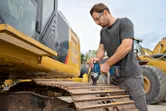 Una persona que usa equipo de seguridad utiliza una llave de impacto inalámbrica en la oruga de una excavadora.