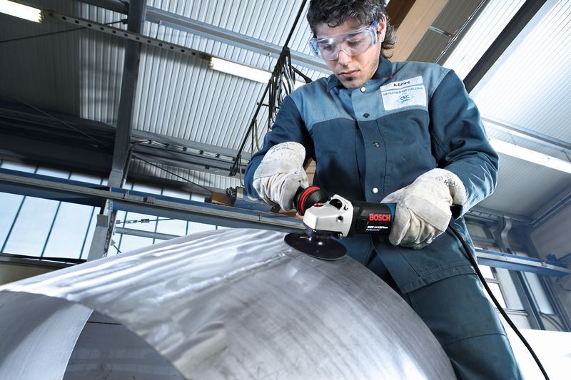 Una persona que usa equipo de seguridad muele una superficie metálica curvada con una amoladora angular.