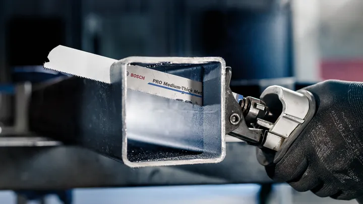 Persona que usa equipo de seguridad y utiliza una sierra alternativa para cortar un tubo de metal.