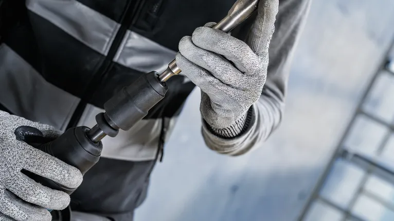 Una persona que usa equipo de seguridad coloca una broca en una herramienta eléctrica.