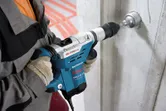 Una persona que usa equipo de seguridad perfora una pared de hormigón con un martillo perforador.