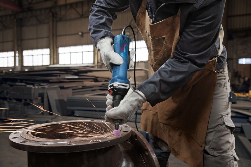 Una persona que usa equipo de seguridad muele metal con una amoladora recta, produciendo chispas.