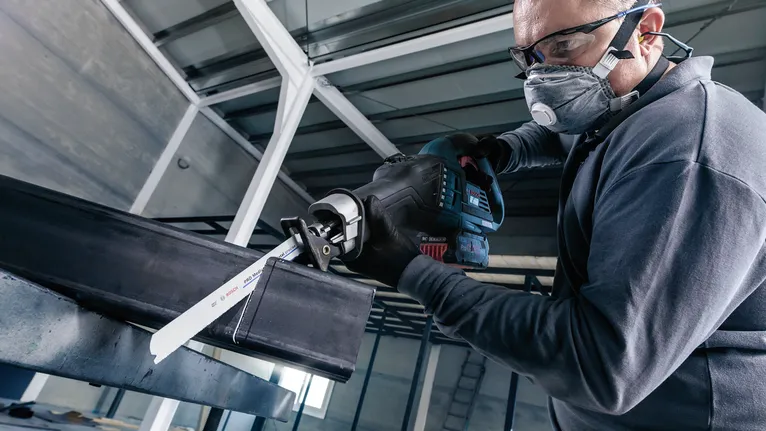 Una persona que usa equipo de seguridad corta una viga de metal con una sierra alternativa.