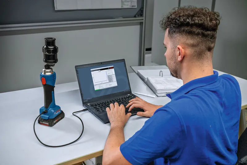 Una persona conecta una herramienta de perforación hidráulica inalámbrica a una computadora portátil en un escritorio.