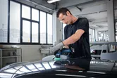 Una persona que usa equipo de seguridad pule el capó de un automóvil en un taller.