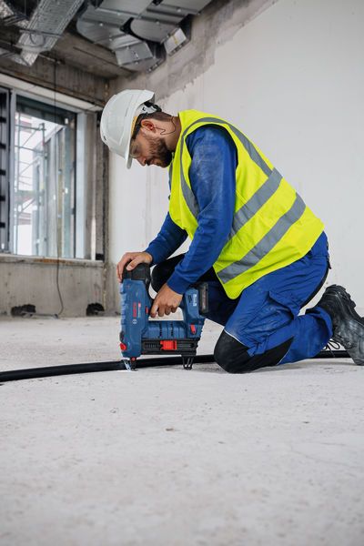 Una persona que lleva equipo de seguridad utiliza una clavadora de hormigón inalámbrica en una obra de construcción.
