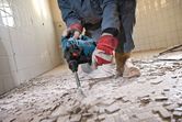 Una persona que usa equipo de seguridad utiliza un martillo demoledor para quitar baldosas del piso.