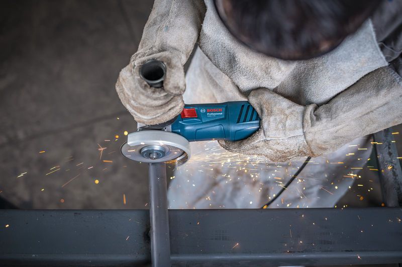 Una persona que usa equipo de seguridad muele tubos de metal con una amoladora angular, lo que produce chispas.