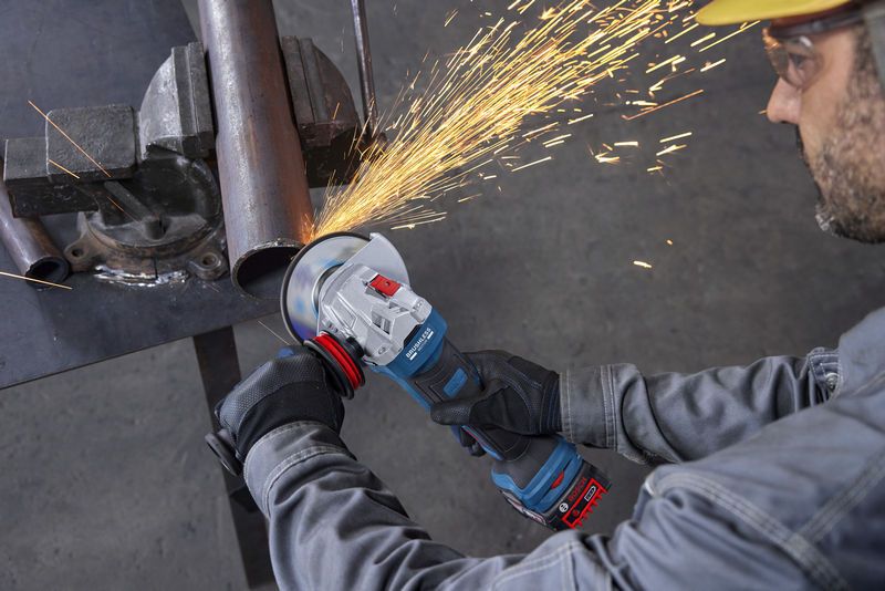 Una persona que usa equipo de seguridad utiliza una amoladora angular para cortar un tubo de metal.