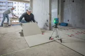 Una persona que lleva equipo de seguridad alinea las baldosas del suelo utilizando una herramienta de nivelación láser.