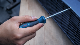 Persona que utiliza un destornillador de mango azul para apretar un tornillo en una rejilla de ventilación metálica.