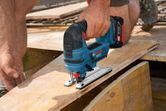 Una persona corta una línea curva en madera contrachapada utilizando una sierra caladora inalámbrica.