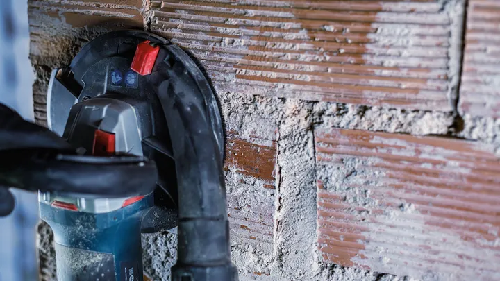 شخص يرتدي معدات السلامة يقوم بحفر أخدود في جدار من الطوب.