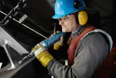 A person wearing safety equipment grinds a metal structure with a straight grinder.