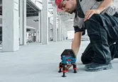 A person wearing safety equipment adjusts a laser leveling tool on a concrete floor.