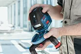 Person in workwear adjusts a laser leveling tool on a tripod indoors.