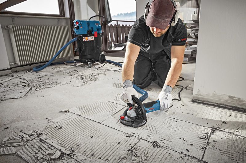 A person wearing safety equipment grinds concrete flooring with a concrete grinder.