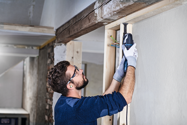 Person wearing safety equipment cuts wood near exposed wires with a power tool.