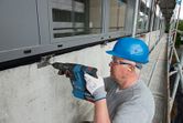 A person wearing safety equipment drills into a concrete wall at a construction site.