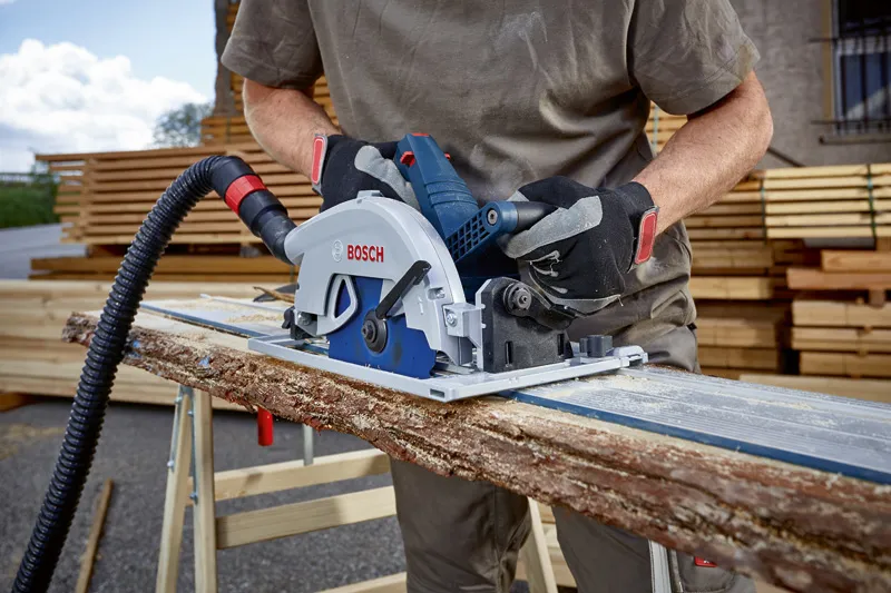 Person wearing safety equipment cuts a rough wooden plank with a circular saw.