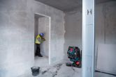 A person wearing safety equipment checks alignment with a laser leveling tool in a room under construction.
