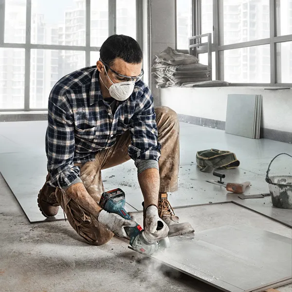 A person wearing safety equipment cuts a tile sheet with a power tool indoors.