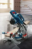 Mitre saw cutting a wooden board on a tiled floor in a modern workspace.