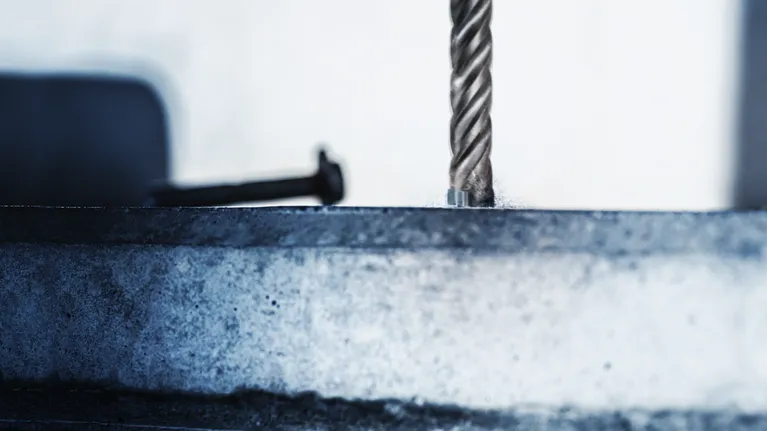 A rotary drill bit making a hole in a metal surface.