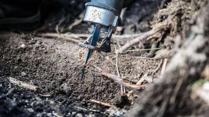 Reciprocating saw cutting through a tree root in the soil.