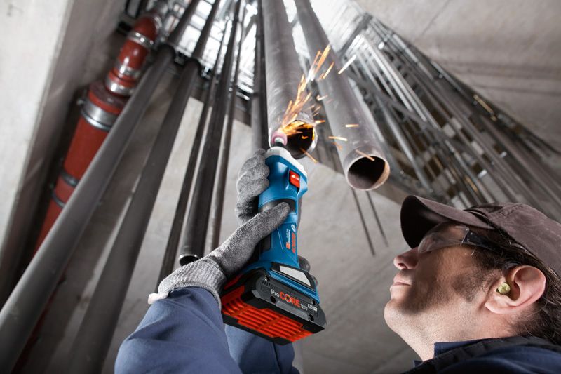 A person wearing safety equipment grinds inside a metal pipe with a cordless straight grinder.
