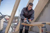 A person wearing safety equipment cuts wood with a circular saw on a construction site.