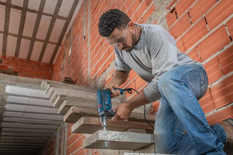 A person wearing safety equipment drills into a concrete staircase with an impact drill.