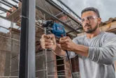 Person wearing safety equipment drills into a metal beam at a construction site.
