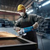 A person wearing safety equipment grinds metal with a power tool, producing sparks.