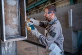 A person wearing safety equipment grinds metal with an angle grinder, producing sparks.