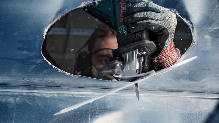 Person wearing safety equipment cuts a large hole in metal with a reciprocating saw.