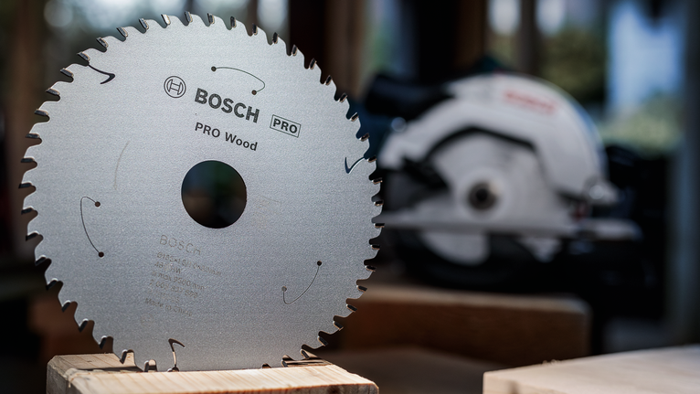 Circular saw blade displayed upright on wood with a power saw in the background.