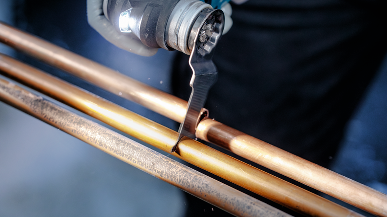 Person using an oscillating tool to cut a copper pipe.