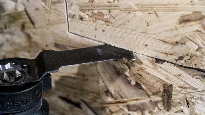 Oscillating tool blade cutting a precise line in oriented strand board.