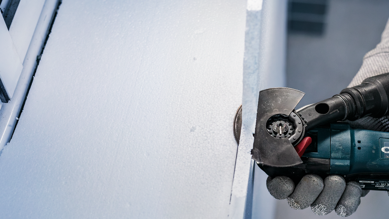 Person wearing safety equipment uses a power tool to cut a sheet of insulation.