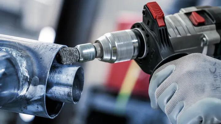 Person wearing safety equipment uses a power drill to grind the inside of a metal pipe.
