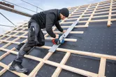 A person wearing safety equipment cuts wood on a steep roof using a cordless circular saw.