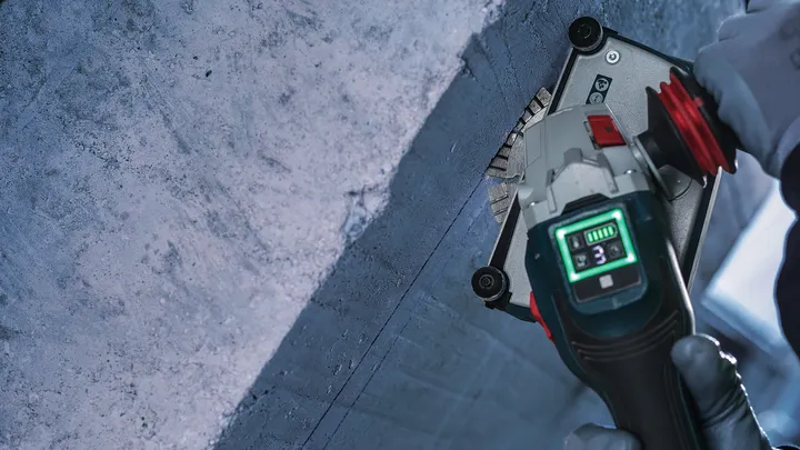 Person wearing safety equipment uses a power tool to cut a groove in concrete.