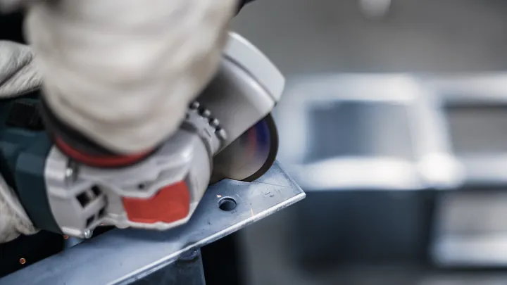 Person wearing safety equipment grinds the edge of a metal plate.