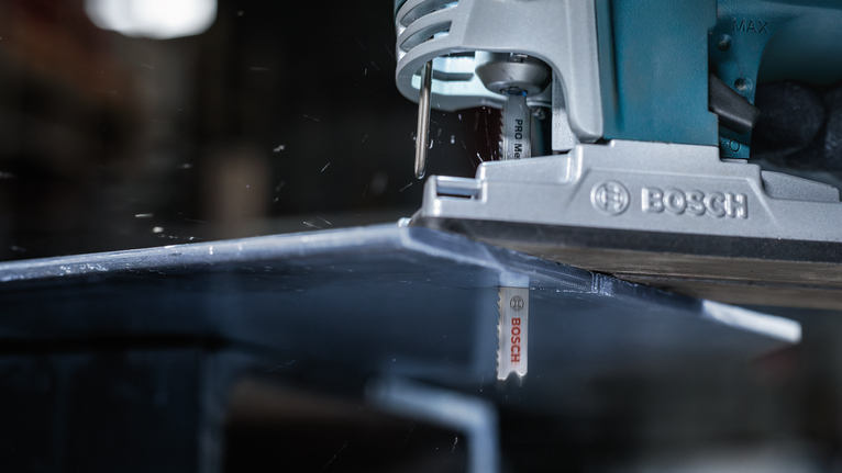 Jigsaw cutting through a metal sheet in a workshop.