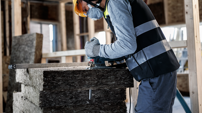 Person wearing safety equipment cuts insulation board with a power tool.